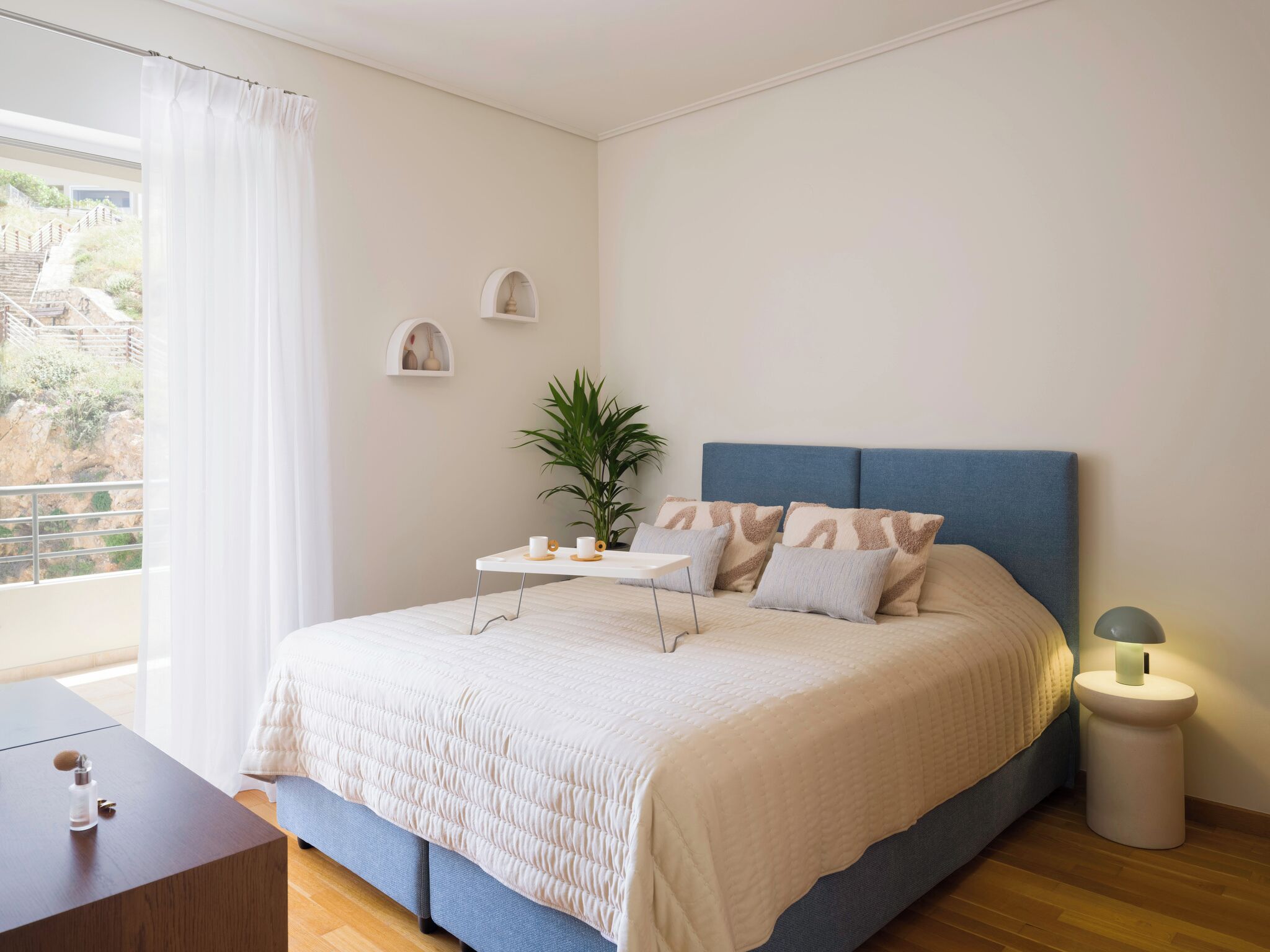 A bedroom with a bed, bedside table, lamp, and a view of the outdoors.