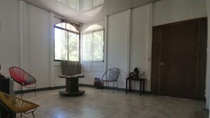 Una habitación amplia con piso de baldosas, dos sillas, una mesa con un altavoz y una puerta de madera grande.