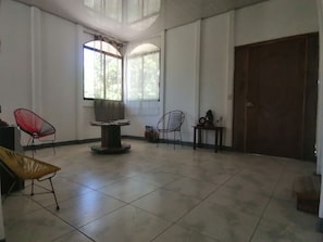 A spacious room with a tiled floor, two chairs, a table with a speaker, and a large wooden door. - Auralivingcr (La Garita)