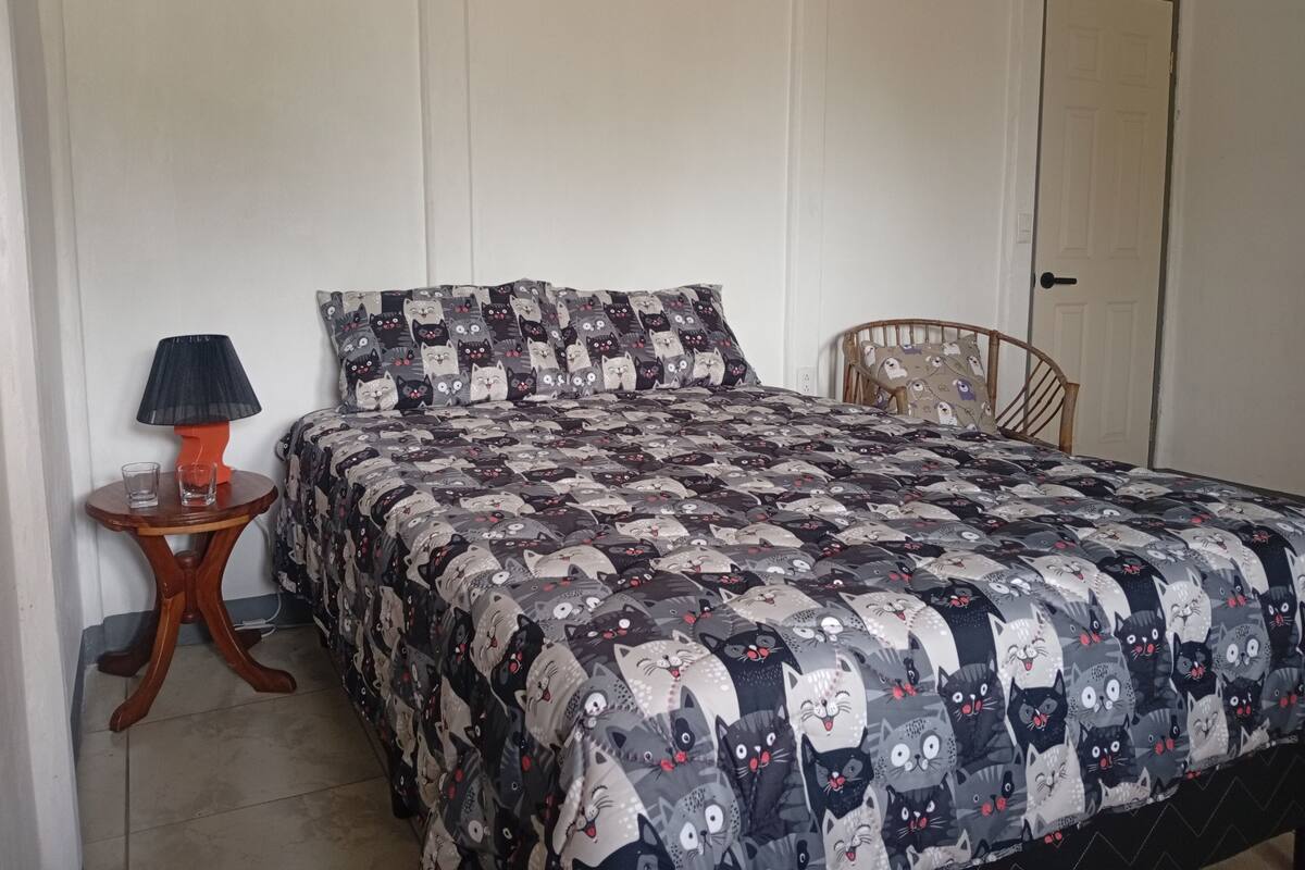 A bed with a patterned quilt, a bedside table with a lamp, and a chair.