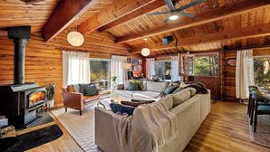 Ein Blockhaussalon mit Kamin, Holzbalkendecke, einer Couch und einem Essbereich.