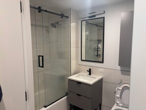 Ein modernes Badezimmer mit einer Duschkabine aus Glas, einem weißen Waschbecken und einem Spiegel darüber.