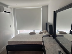 Ein modernes Schlafzimmer mit einem Bett, einem großen Spiegel und einem Fenster mit Jalousien.