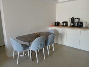 A dining area with a glass table and four chairs, a white cabinet with kitchen appliances, and a small decorative item on the table.