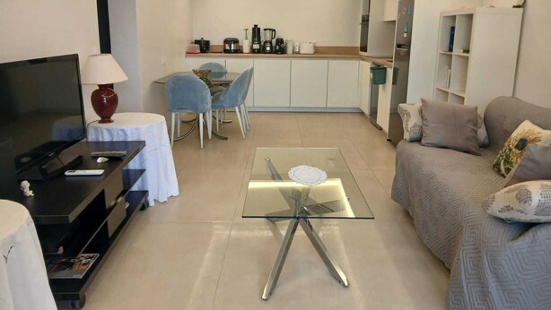 Ein modernes Wohnzimmer mit Fernseher, einer Couch, einem Glastisch und einem Essbereich mit Stühlen und Tisch.