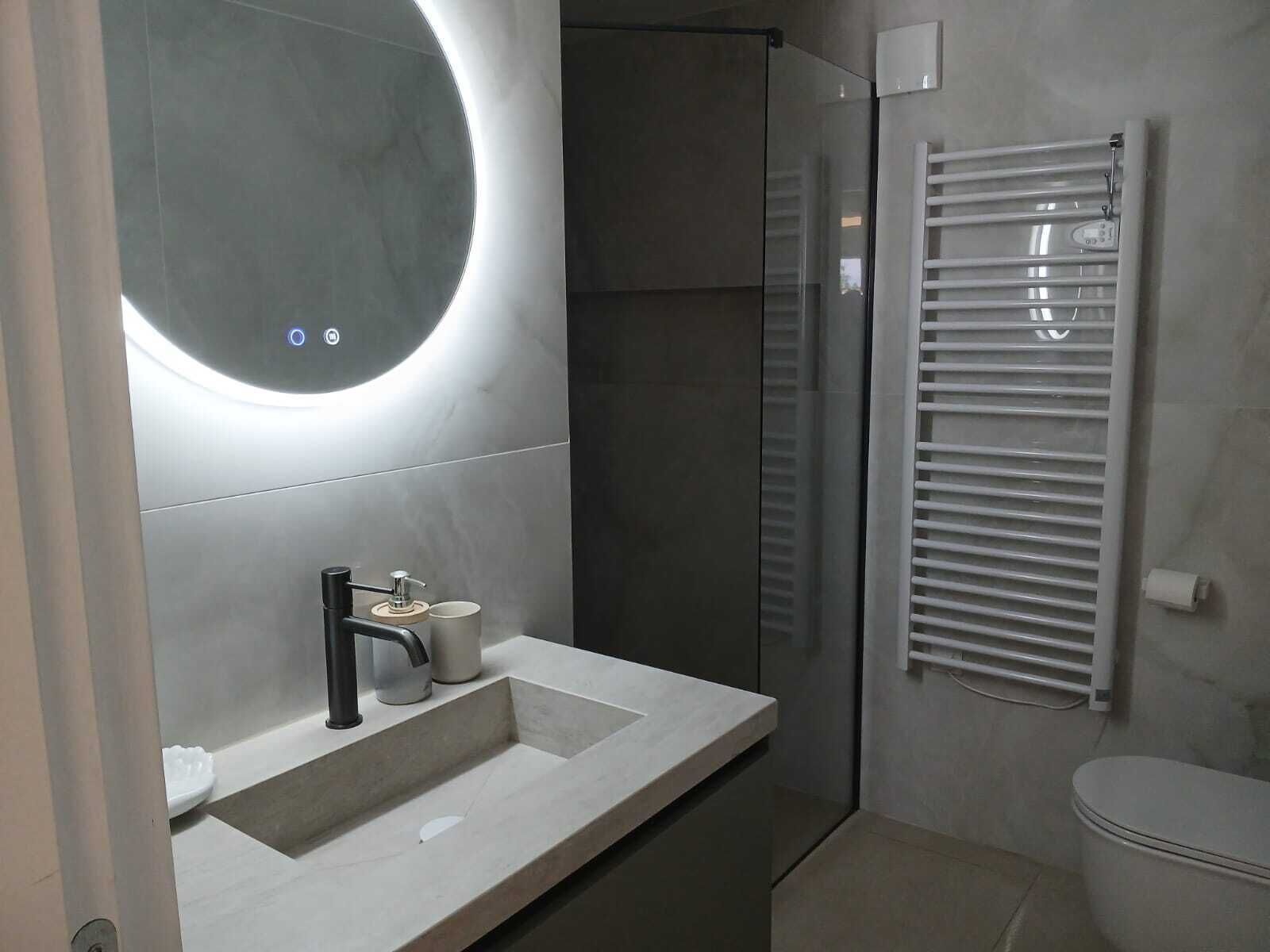 A modern bathroom with a round mirror, a sink, a toilet, and a glass shower enclosure.