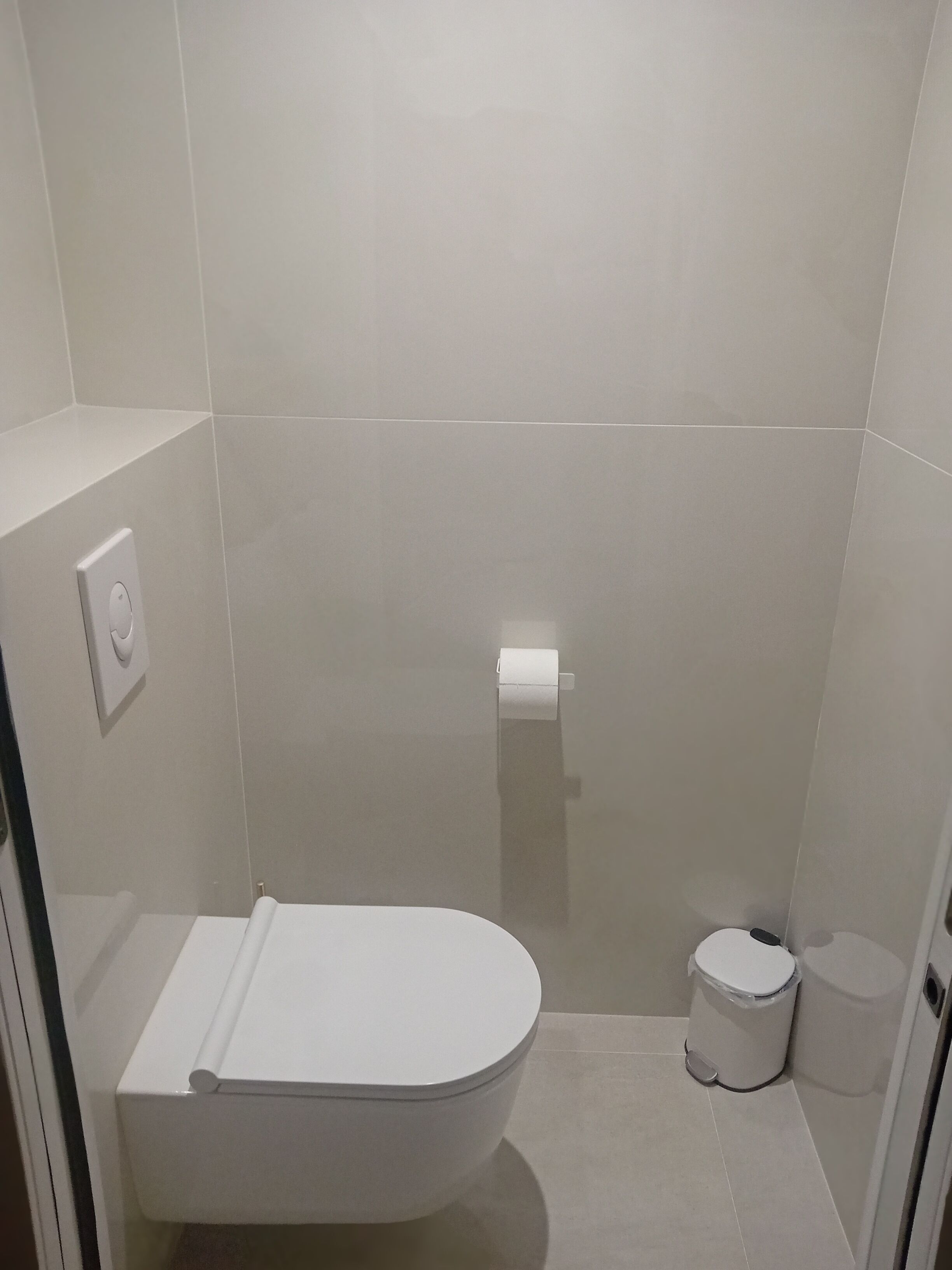 Un baño moderno con inodoro, un cubo de basura y un dispensador de papel higiénico en la pared.
