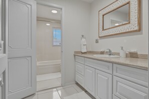 A bathroom with a bathtub, a sink, a mirror, and a towel rack.