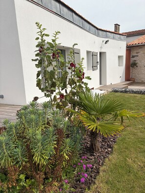 A modern building with a white exterior, a stone wall, and a garden with various plants and flowers.