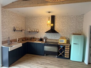 A kitchen with a stone wall, wooden beams, a built-in oven, a microwave, and a wine rack.