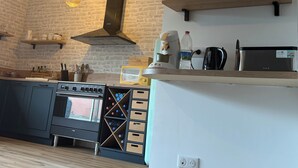 Ett kök med spis, ugn och kaffebryggare, synliga träbjälkar, en hängande lampa och en målning av en segelbåt på väggen.