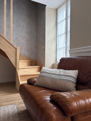 Ein braunes Ledersofa mit Kissen, eine Holztreppe und ein Fenster mit Vorhängen.