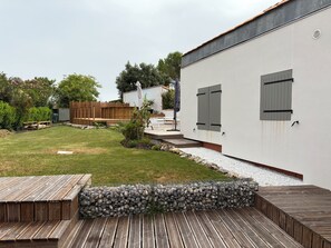 Eine moderne Terrassenanlage im Freien mit Holzboden, Steinrand und einem weiß gestrichenen Gebäude mit Fensterläden.