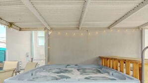 Et spabad med træterrasse, betonvæg og lyskæder.