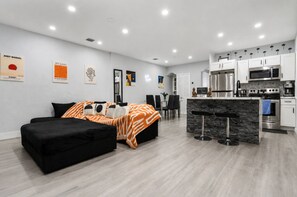 A modern apartment with a black sofa, a kitchen with white cabinets, and artwork on the walls. - Arcade + Plunge Pool - Calle Ocho Near Brickell (Miami)