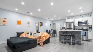 En moderne lejlighed med en sort sofa, et sengetæppe med zebra-mønster, et køkken med hvide skabe og kunst på væggene.