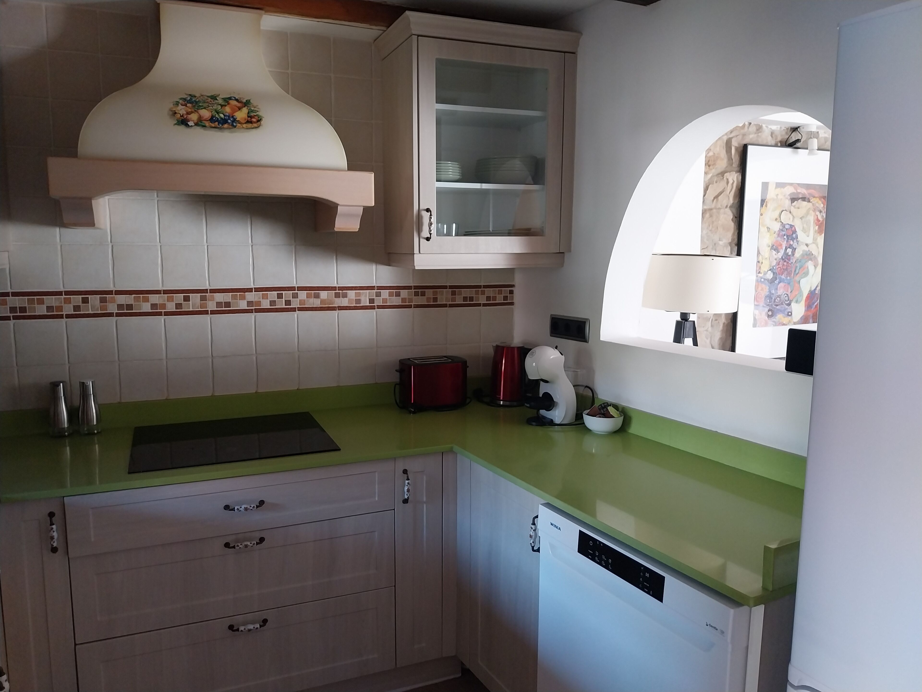 A kitchen with a green countertop, white cabinets, a toaster, a kettle, and a microwave.