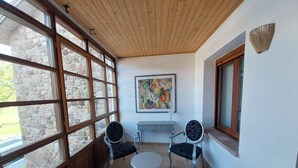 Een kamer met een stenen muur, houten plafond, twee stoelen, een klein tafeltje en een schilderij.