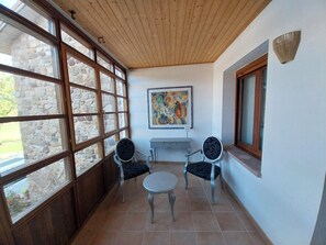 A room with a stone wall, wooden ceiling, two chairs, a small table, and a painting.