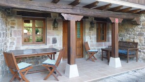 Een stenen gebouw met een houten veranda, een tafel, twee stoelen en een bank.