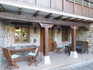 A stone building with a wooden porch, a table, two chairs, and a bench.