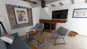 Een woonkamer met een bank, twee fauteuils, een salontafel, een open haard, een televisie en een accentmuur van steen.