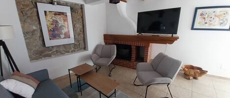 A living room with a sofa, two armchairs, a coffee table, a fireplace, a TV, and a stone accent wall.