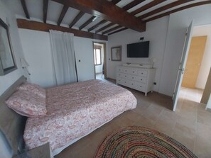 A bedroom with a bed, a dresser, a television, and a door leading to another room.