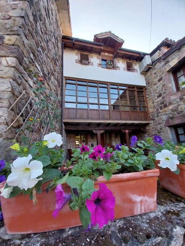 A building with a stone facade, a wooden balcony, and flower planters with various flowers.