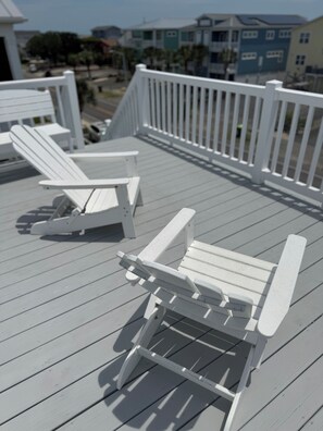 Eine Terrasse mit weißen Adirondack-Stühlen, einem weißen Geländer und Blick auf Gebäude im Hintergrund.