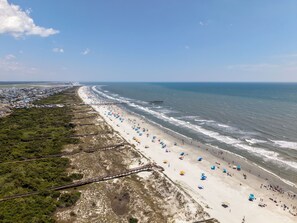 A coastal beach with a wooden boardwalk, beach umbrellas, and a pier. - Second Row Sunset Beach Island West    Coastal Escape 
Luxury Beach House (Sunset Beach)
