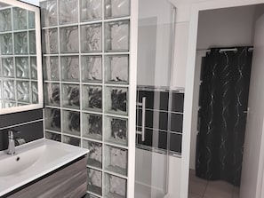 Ein Badezimmer mit Duschkabine aus Glas, einem weißen Waschbecken und einer gefliesten Wand mit Marmormuster.