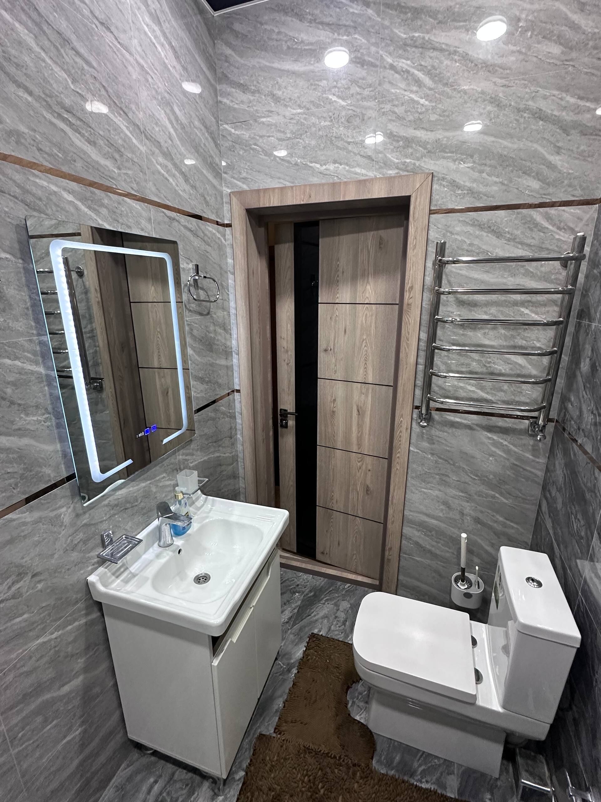 Un baño con pared de mármol, un lavamanos, un inodoro, un espejo y un perchero para toallas.