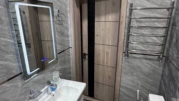 Un baño con pared de mármol, un lavamanos, un inodoro, un espejo y un perchero para toallas.