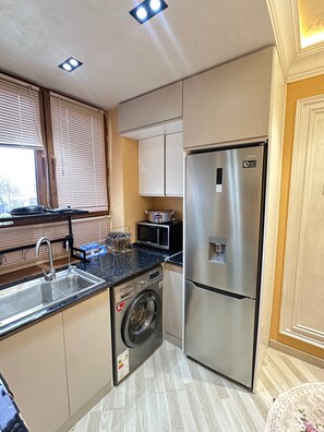 A compact kitchen with a stainless steel refrigerator, a washing machine, a microwave, and a sink. - Charming 3-bedroom apartment with AC & fast Wi-Fi in Samarkand (Samarkand)