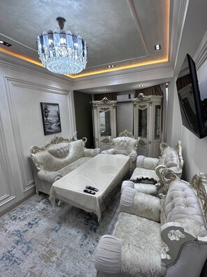 A luxurious bedroom with a large bed, ornate furniture, a chandelier, and a television mounted on the wall.