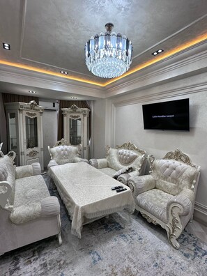 A luxurious room with a large chandelier, ornate furniture, a flat-screen TV, and a patterned carpet.