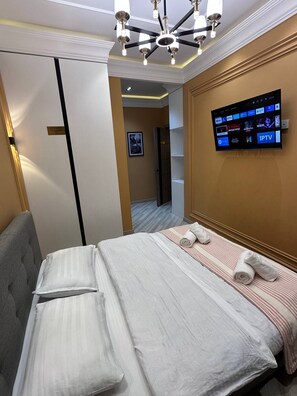 A hotel room with a bed, a television mounted on the wall, a chandelier, and a door.