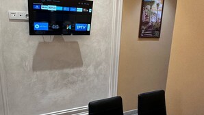 Un comedor con una mesa redonda preparada para cuatro personas, un televisor de pantalla plana en la pared y un cuadro enmarcado.