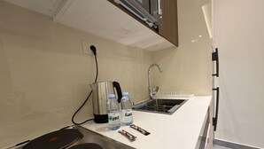 Una kitchenette con estufa, hervidor, pileta y una encimera con botellas de agua y una barra de chocolate.