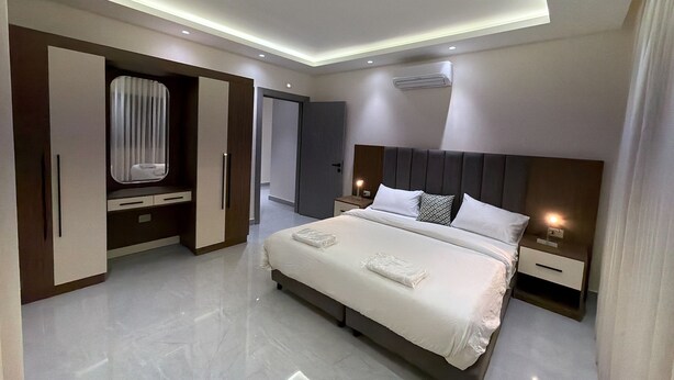 Una habitación de hotel moderna con una cama grande, mesitas de noche, un armario y una lámpara de techo.