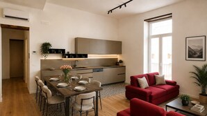 A modern living space with a dining area, a red sofa, and a kitchen with a built-in oven. - Penthouse Napoli Terrace-Dante Rooftop (Naples)