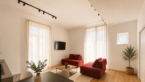 Ein modernes Wohnzimmer mit einer Couch, einem an der Wand befestigten Fernseher und einem Essbereich mit Tisch und Stühlen.