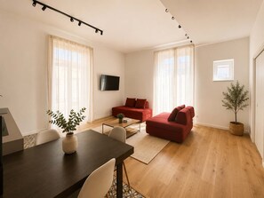 A modern living room with a sofa, a TV mounted on the wall, and a dining area with a table and chairs. - Family & Friends Wing at Penthouses Dante. Private wing for groups: 35sqm kitchen/lounge, 3 ensuite bedrooms—30sqm Suite with balcony on Piazza Dante, 20sqm Superior, and a Double room. Access to panoramic rooftop over historic center's ancient domes. (Naples)