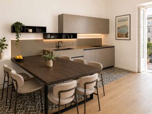 A modern kitchen with a dark wooden table, light-colored chairs, and a built-in oven. - Family & Friends Wing at Penthouses Dante. Private wing for groups: 35sqm kitchen/lounge, 3 ensuite bedrooms—30sqm Suite with balcony on Piazza Dante, 20sqm Superior, and a Double room. Access to panoramic rooftop over historic center's ancient domes. (Naples)