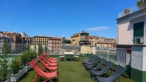 Eine Dachterrasse mit künstlichem Gras, roten und grauen Liegestühlen und Blick auf historische Gebäude.