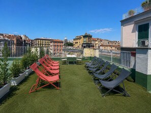 A rooftop terrace with artificial grass, red and grey lounge chairs, and a view of historic buildings. - Family & Friends Wing at Penthouses Dante. Private wing for groups: 35sqm kitchen/lounge, 3 ensuite bedrooms—30sqm Suite with balcony on Piazza Dante, 20sqm Superior, and a Double room. Access to panoramic rooftop over historic center's ancient domes. (Naples)