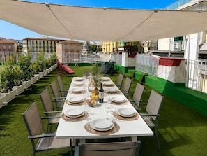 An outdoor dining area with a long table set for a meal, surrounded by chairs and a canopy. - Family & Friends Wing at Penthouses Dante. Private wing for groups: 35sqm kitchen/lounge, 3 ensuite bedrooms—30sqm Suite with balcony on Piazza Dante, 20sqm Superior, and a Double room. Access to panoramic rooftop over historic center's ancient domes. (Naples)