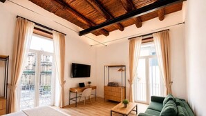 Ein Hotelzimmer mit einem Bett, einem Schreibtisch mit Laptop, einem grünen Sofa und einem an der Wand montierten Fernseher.