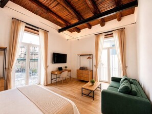 A hotel room with a bed, a desk with a laptop, a green sofa, and a TV on the wall. - Family & Friends Wing at Penthouses Dante. Private wing for groups: 35sqm kitchen/lounge, 3 ensuite bedrooms—30sqm Suite with balcony on Piazza Dante, 20sqm Superior, and a Double room. Access to panoramic rooftop over historic center's ancient domes. (Naples)